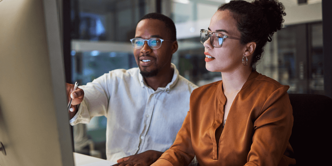 Two coworkers reviewing data at a desktop computer 