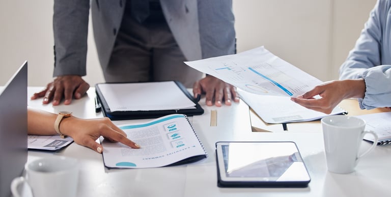 A photo of paperwork and a tablet on top of a table and a few hands going trough it all