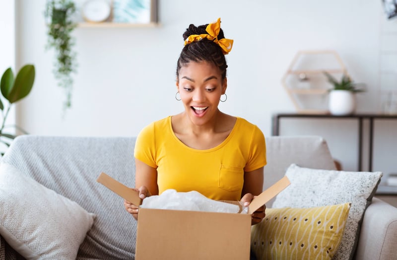 Women unboxing a gift sitting in her couch and looking surprised