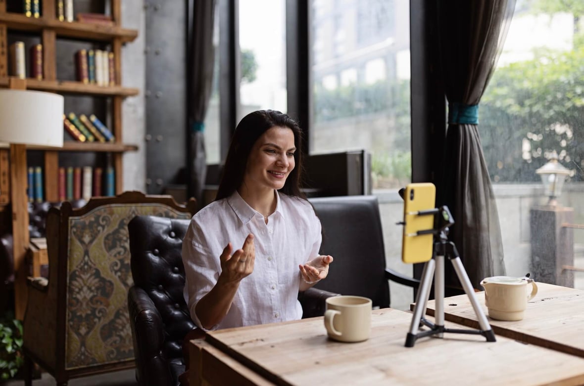 women sitting at a desk recording a video from her phone