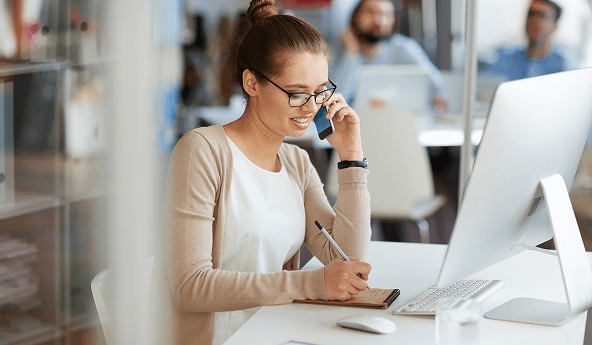 Female marketer at the office, sitting at her desk talking on a cell phone