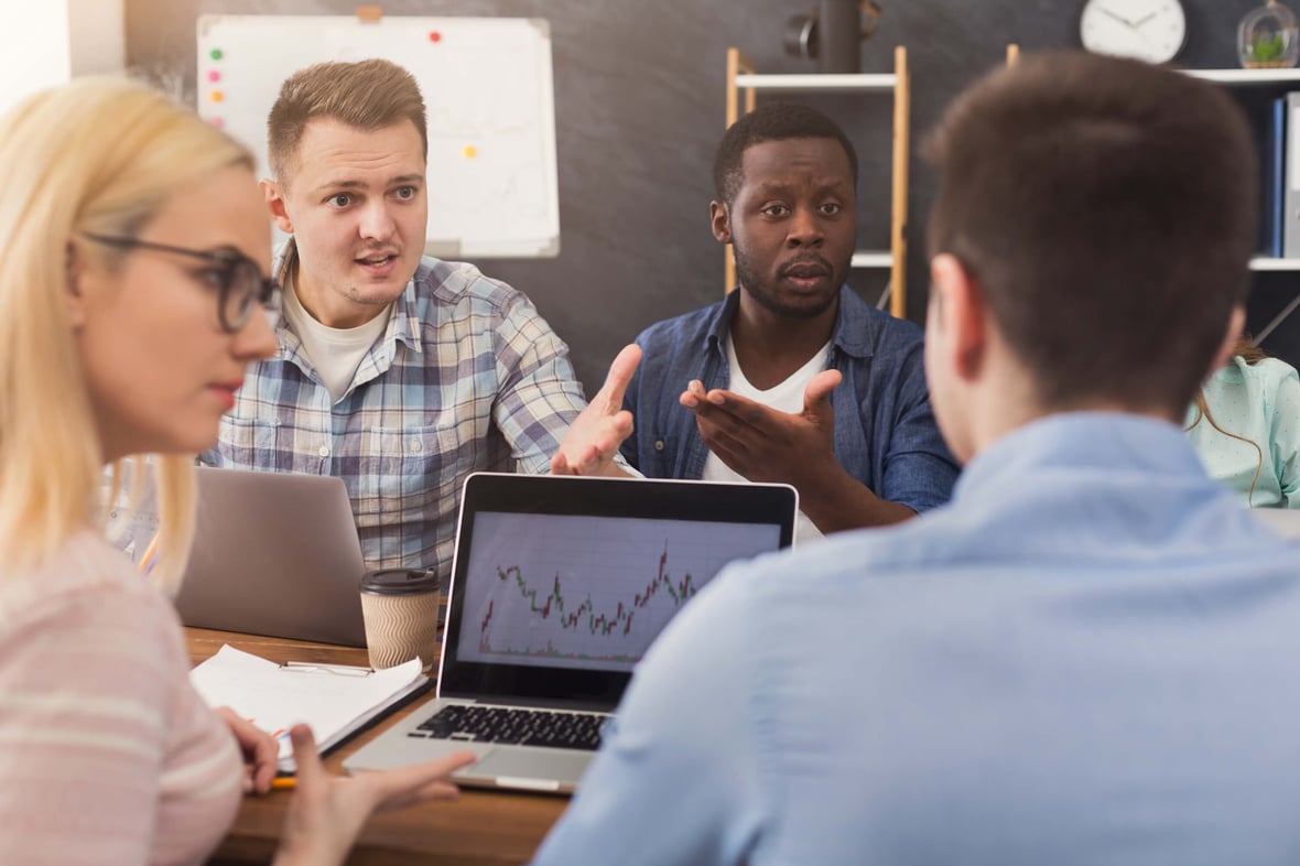 Marketers discussing leads around a meeting table with laptops