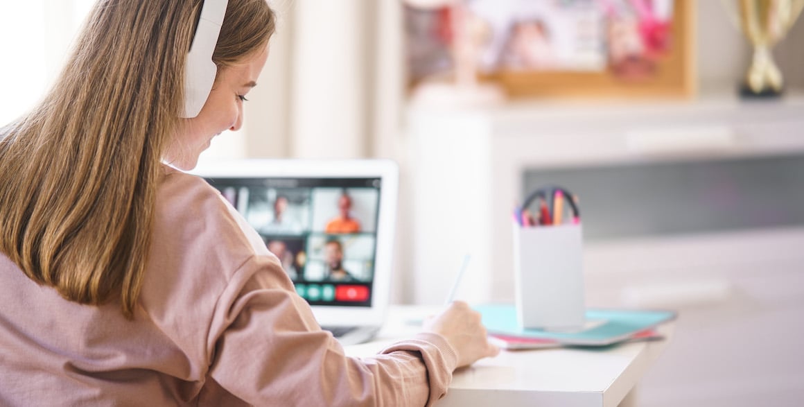 Young adult on computer video call with multiple people and taking analog notes 