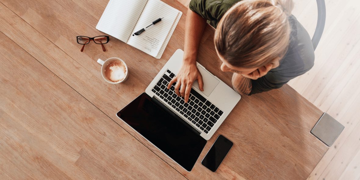 Woman looking at a laptop with a notebook and coffee