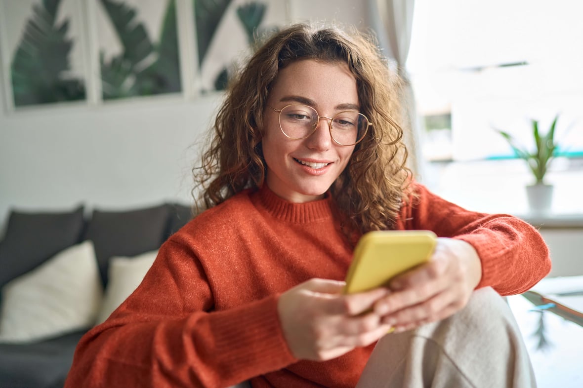 Woman sitting at her desk smiling and browsing content on her cellphone