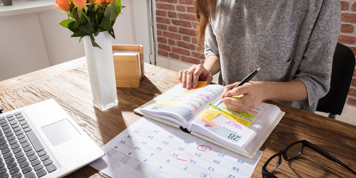 Close up image showing the hands of a woman writing on an agenda with a calendar