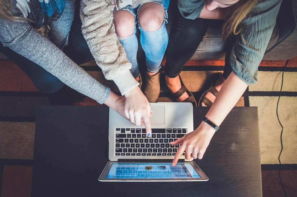 Close up shot into a group of three people pointing at a laptop