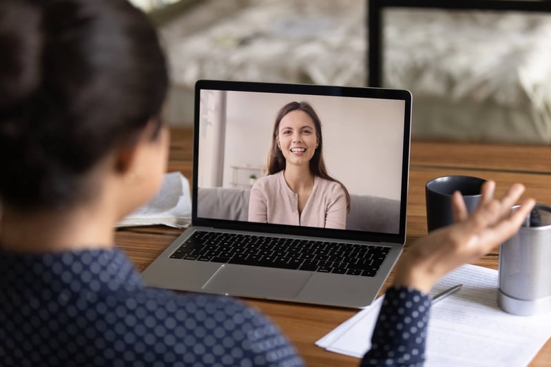 Two women, one in person and one on a laptop, on a virtual job interview.