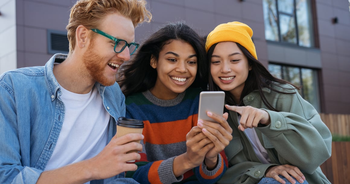 three young adults looking at a smart phone and smiling
