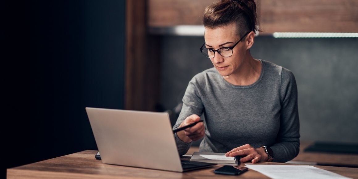 Woman looking at a laptop sand pointing a pen at the screen