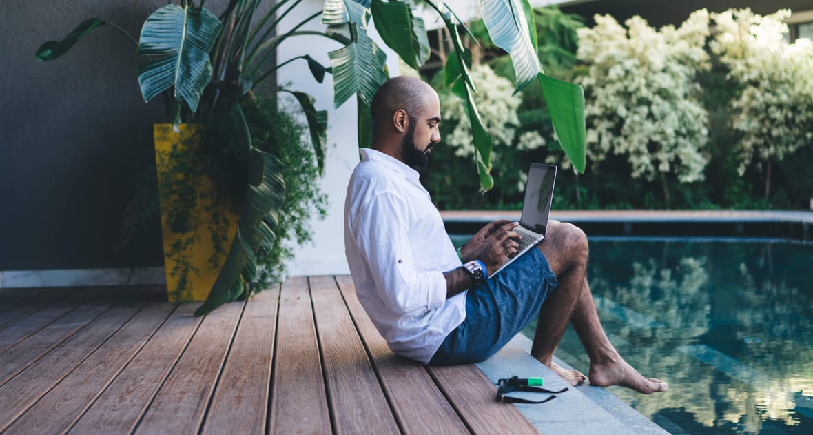 Man working  remotely with his laptop at the side of a pool