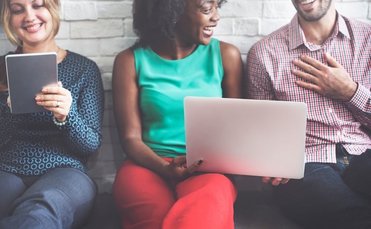 Two woman and a man sitting on a bench and looking at a laptop