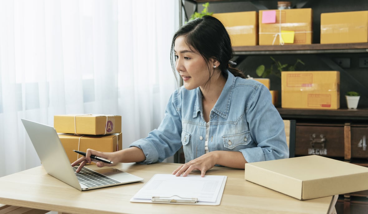 Asian woman working on laptop and preparing orders for her E-Commerce store