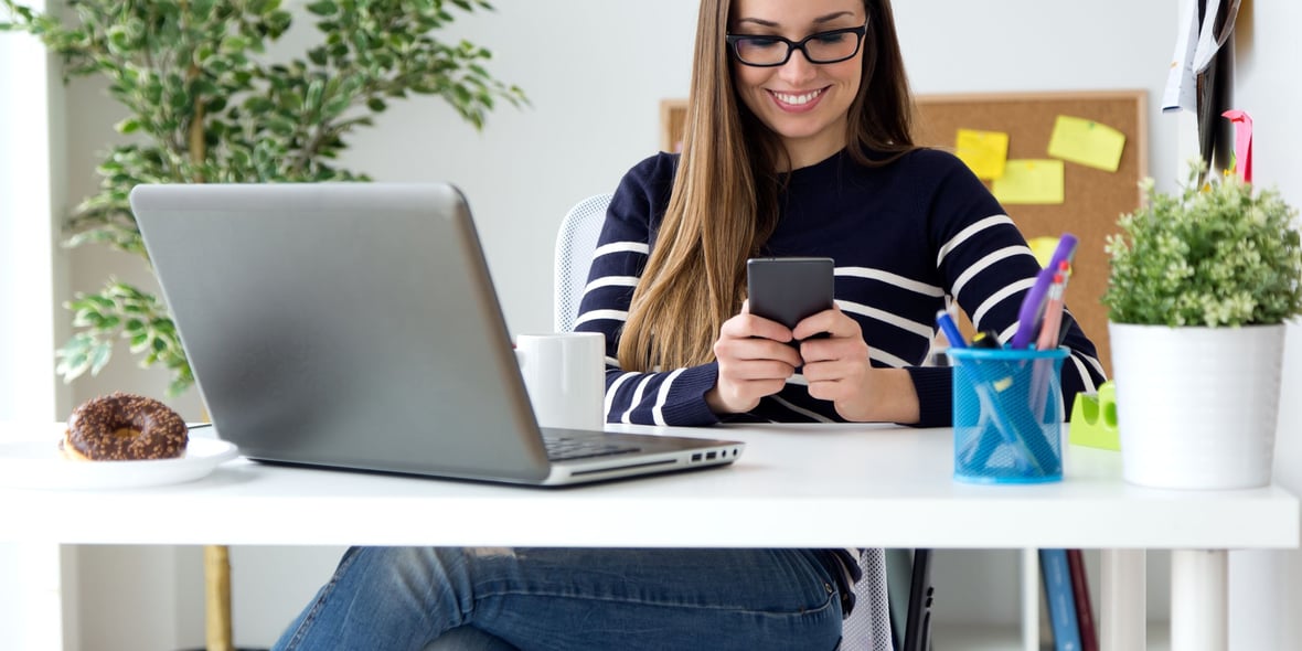 Woman sitting at a desk and looking at her phone while smiling