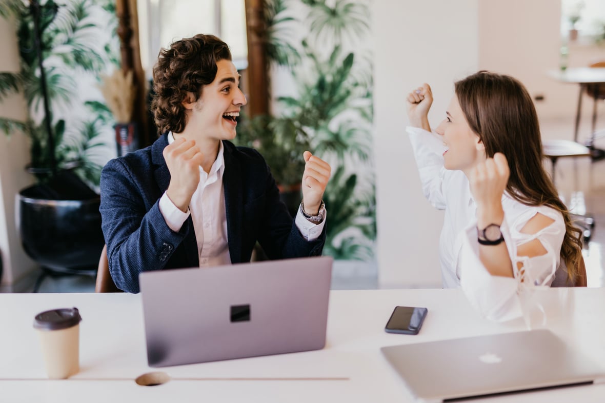 Two marketers smiling at each other and raising their hands while looking at a computer screen