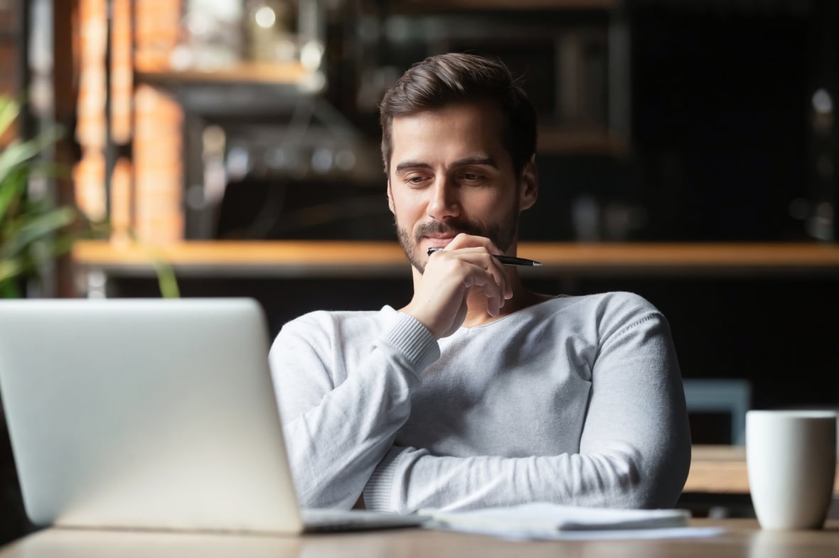 Man looking at a laptop while holding a pen on his hand