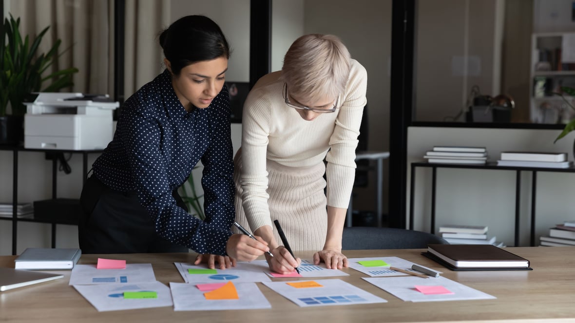 Two marketers leaning over a desk looking at the paperwork on top of it