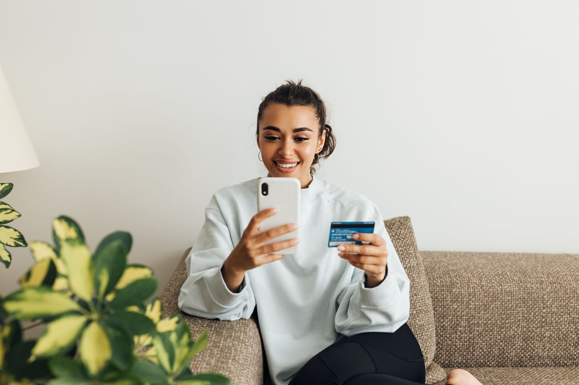 Woman browsing on her phone while holding a credit card on her other hand.