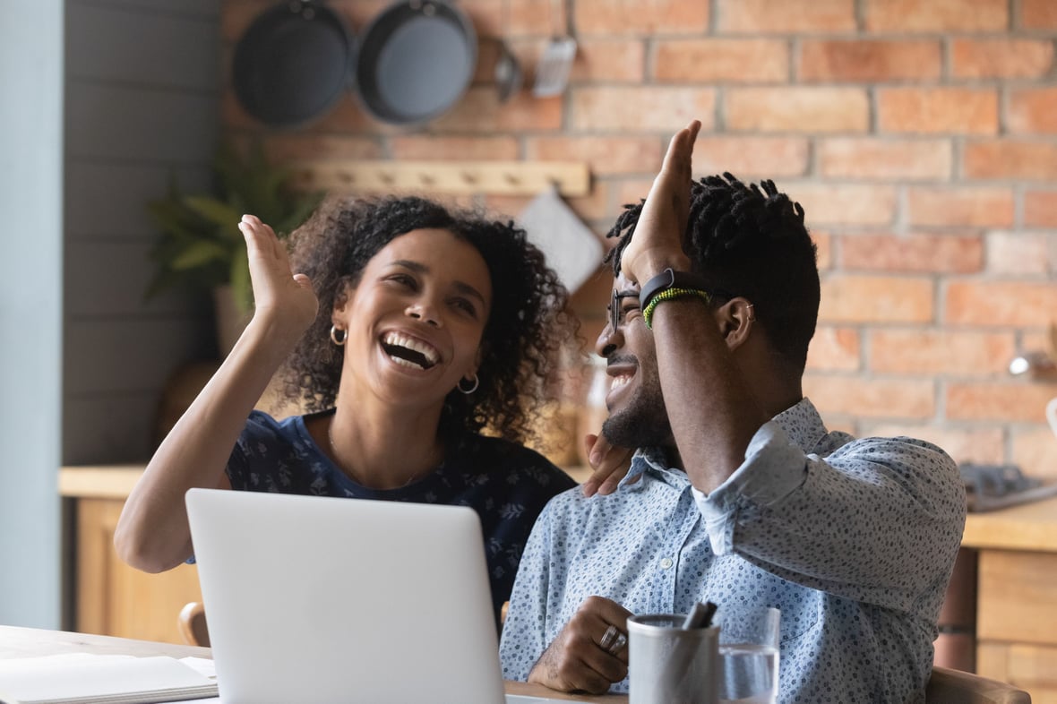 Two marketers smiling at each other while doing a high five in front of a laptop