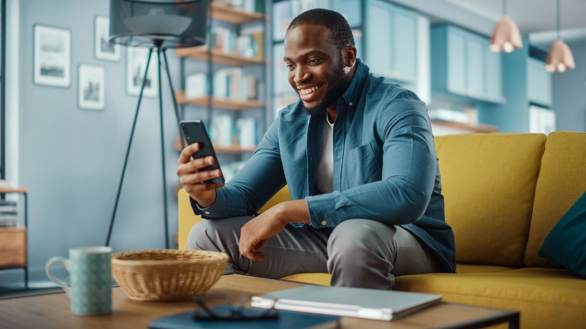 Man looking at his phone while smiling and sitting on his living room