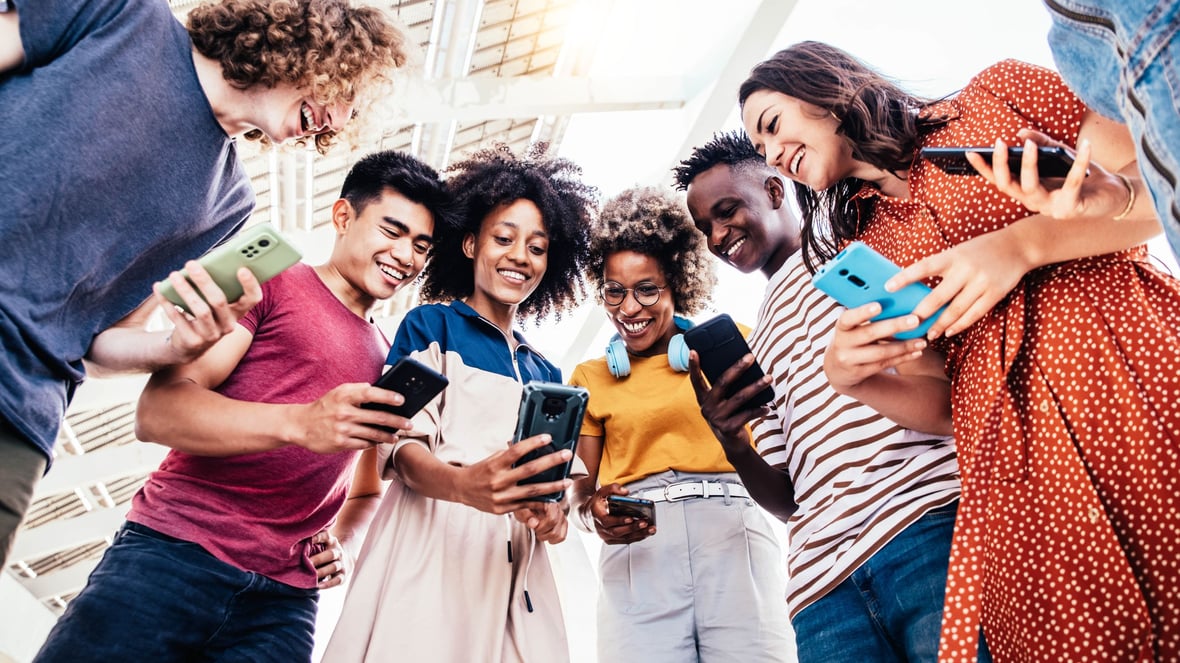 A group of people gathered holding their phones and looking at one of the screens