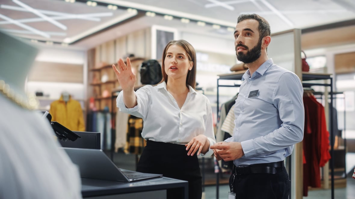 Two workers at a retail store looking at a computer and the products they're selling