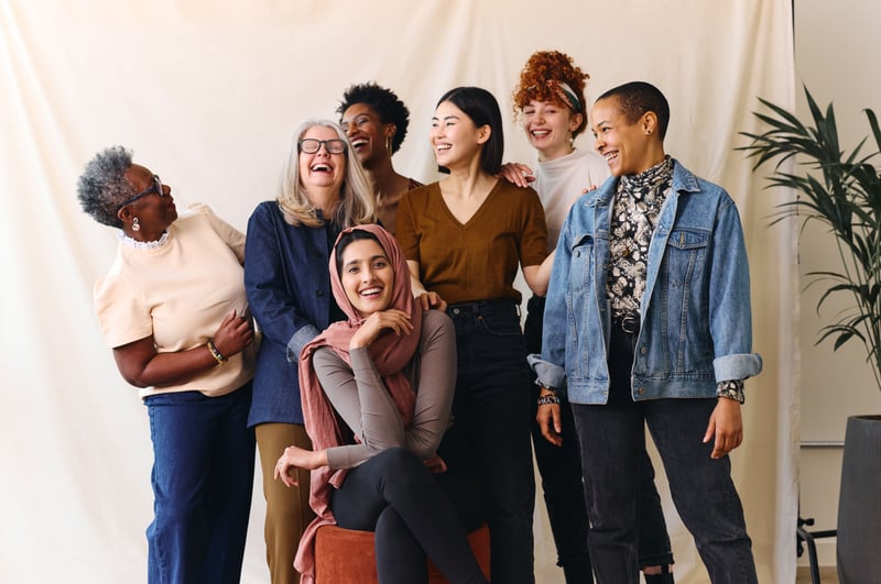 A group of women from different ethnicities and ages laughing on a photoshoot