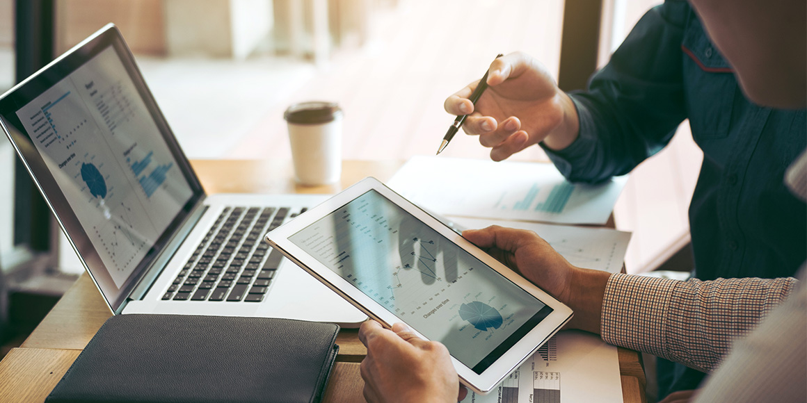 Person working on laptop and iPad to report on leads, MQLs, and SQLs in HubSpot. 