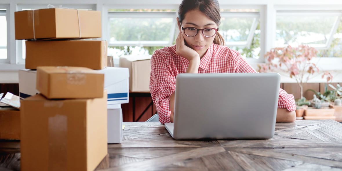 Woman working on her laptop with a pile of product boxes to her side