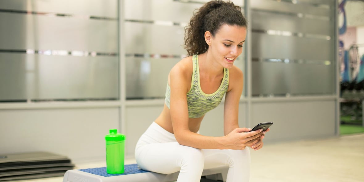 Woman sitting on a gym bench while looking at her phone