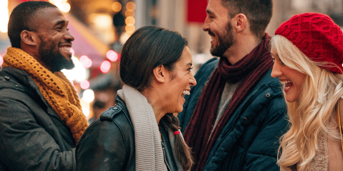 A group of friends laughing with Holiday lights in the background 