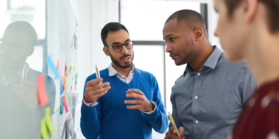 Two men discussing business strategy by whiteboard.