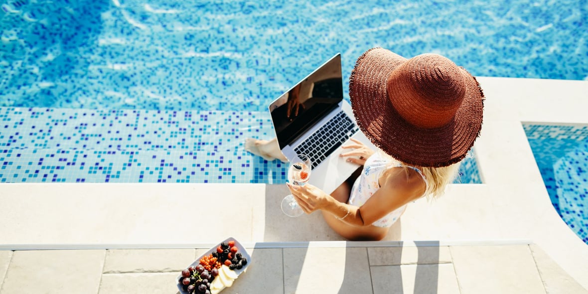 Woman working on a laptop by the side of a pool