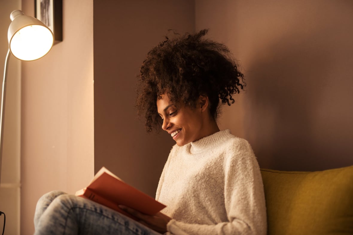 African American Woman Reading a Book on a Yellow Couch 