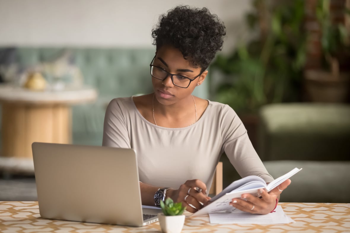 Woman looking at a laptop while holding a notepad open 