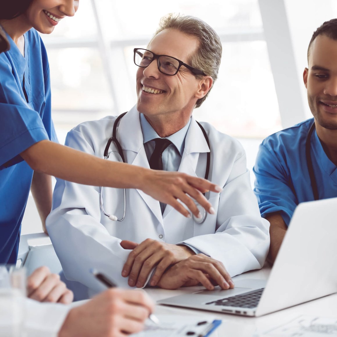 Doctor speaking with healthcare staff while working on a laptop