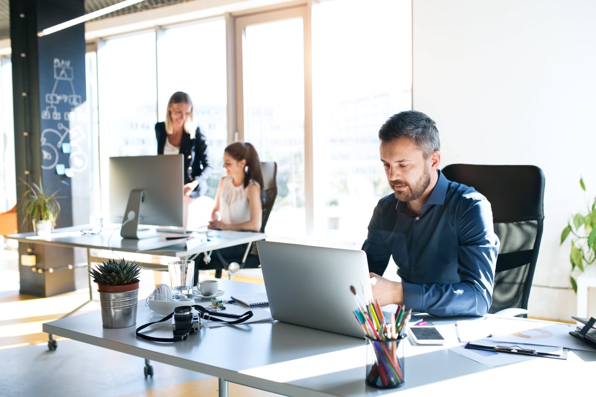 Three marketers in an office siting at their desks and looking at their computer screens